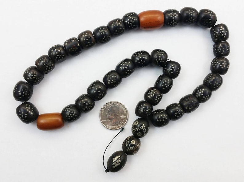 Pu&ograve; includere: Una collana di perline nere e argentate con due perline di legno marrone. La collana &egrave; composta da perline rotonde con un motivo di piccoli punti argentati.