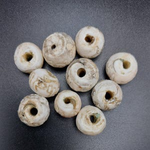 Puede incluir: Diez cuentas de ágata blanca con un agujero en el centro. Las cuentas tienen un patrón de remolino y son ligeramente translúcidas.
