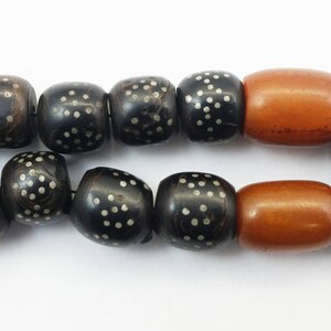 Pu&ograve; includere: Una collana di perline nere e marroni con accenti argentati. La collana ha due grandi perline ambrate.