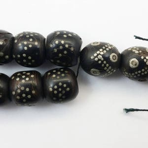 Pu&ograve; includere: Una collana di perle nere con accenti argentati. Le perle sono rotonde e hanno un motivo geometrico. La collana &egrave; infilata su un cordoncino nero.