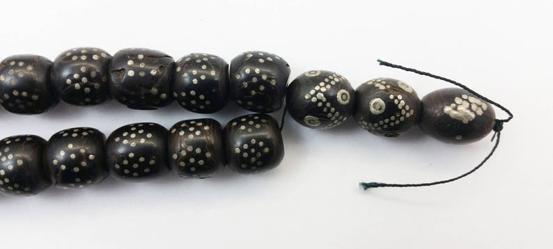 Pu&ograve; includere: Una collana di perle nere con accenti argentati. Le perle sono rotonde e hanno un motivo geometrico. La collana &egrave; infilata su un cordoncino nero.