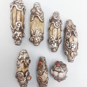 Puede incluir: Siete cuentas de hueso con detalles plateados y piedras preciosas rojas y turquesas. Las cuentas son de forma ovalada y tienen diseños intrincados.