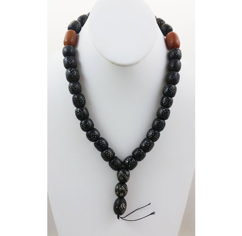 Pu&ograve; includere: Una collana di perline nere con accenti argentati e due perline di legno marrone. La collana ha un fiocco all'estremit&agrave;.
