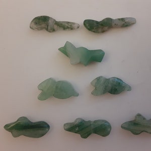 May include: Eight green jade stone carvings of various fish shapes. The carvings are smooth and polished, with a light green color and white streaks.
