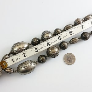May include: A silver necklace with large, ornate beads. The necklace is 7 inches long and features a large, round pendant with intricate designs. The necklace is made in Shanghai, China.