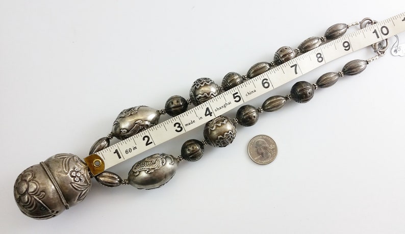 May include: A silver necklace with large, ornate beads. The necklace is 7 inches long and features a large, round pendant with intricate designs. The necklace is made in Shanghai, China.