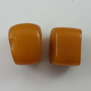 May include: Two amber-colored, square-shaped beads. The beads are smooth and have a slightly glossy finish.