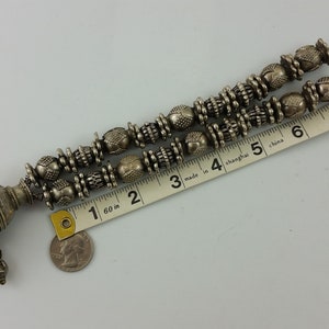 May include: A silver necklace with a large, ornate pendant and multiple strands of beads. The necklace is approximately 23 cm long.