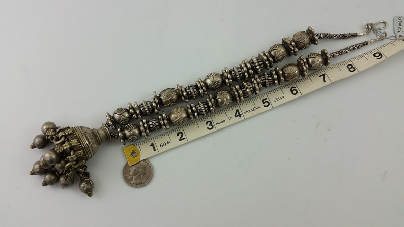 May include: A silver necklace with a large, ornate pendant and multiple strands of beads. The necklace is approximately 23 cm long.