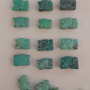 Puede incluir: Una colección de cuentas de piedra tallada de color turquesa. Las cuentas son rectangulares con una forma de animal estilizada. El color varía de turquesa claro a oscuro, con algunos que muestran patrones de matriz más oscuros. Las cuentas están dispuestas en filas.