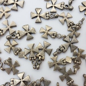 May include: A collection of silver-toned metal cross charms with a decorative design. The charms are linked together with small metal rings.