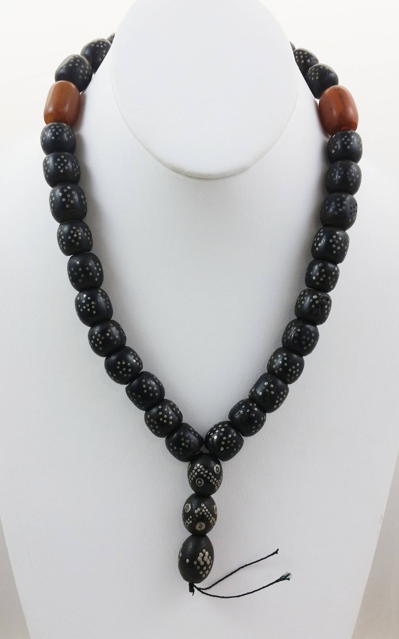 Pu&ograve; includere: Una collana di perline nere con accenti argentati e due perline marroni alle estremit&agrave;. La collana ha un fiocco in basso.