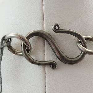 May include: A silver necklace with a detailed, textured design. The necklace has a lobster claw clasp.