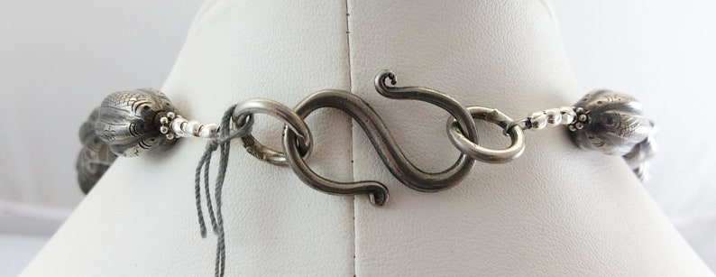 May include: A silver necklace with a detailed, textured design. The necklace has a lobster claw clasp.