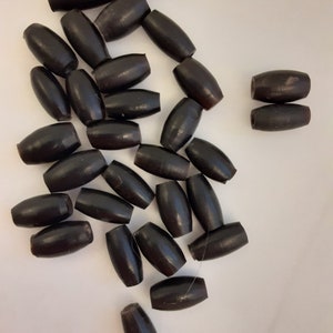 May include: A pile of black wooden beads, some are oval shaped and some are round. The beads are scattered on a white surface.