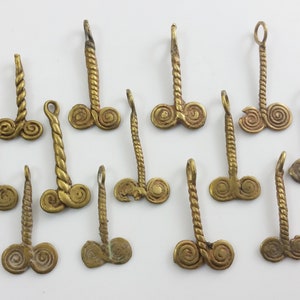 Könnte beinhalten: Zwölf goldfarbene Metallanhänger mit einem gedrehten Seil-Design und einer doppelten Spirale am unteren Ende.