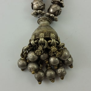 May include: A silver necklace with a pendant featuring a small vase with a chain and multiple silver beads hanging from it.