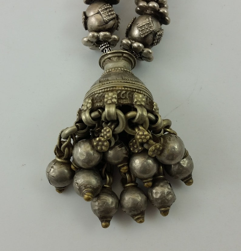 May include: A silver necklace with a pendant featuring a small vase with a chain and multiple silver beads hanging from it.