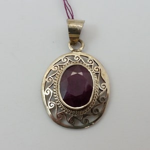 Puede incluir: Un colgante de plata con una piedra preciosa ovalada de color púrpura engastada en un diseño de filigrana.