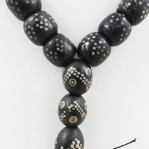 Pu&ograve; includere: Una collana di perline di legno nero con intarsi in argento. Le perline sono di forma ovale e hanno un motivo geometrico. La collana &egrave; infilata su un cordoncino nero.