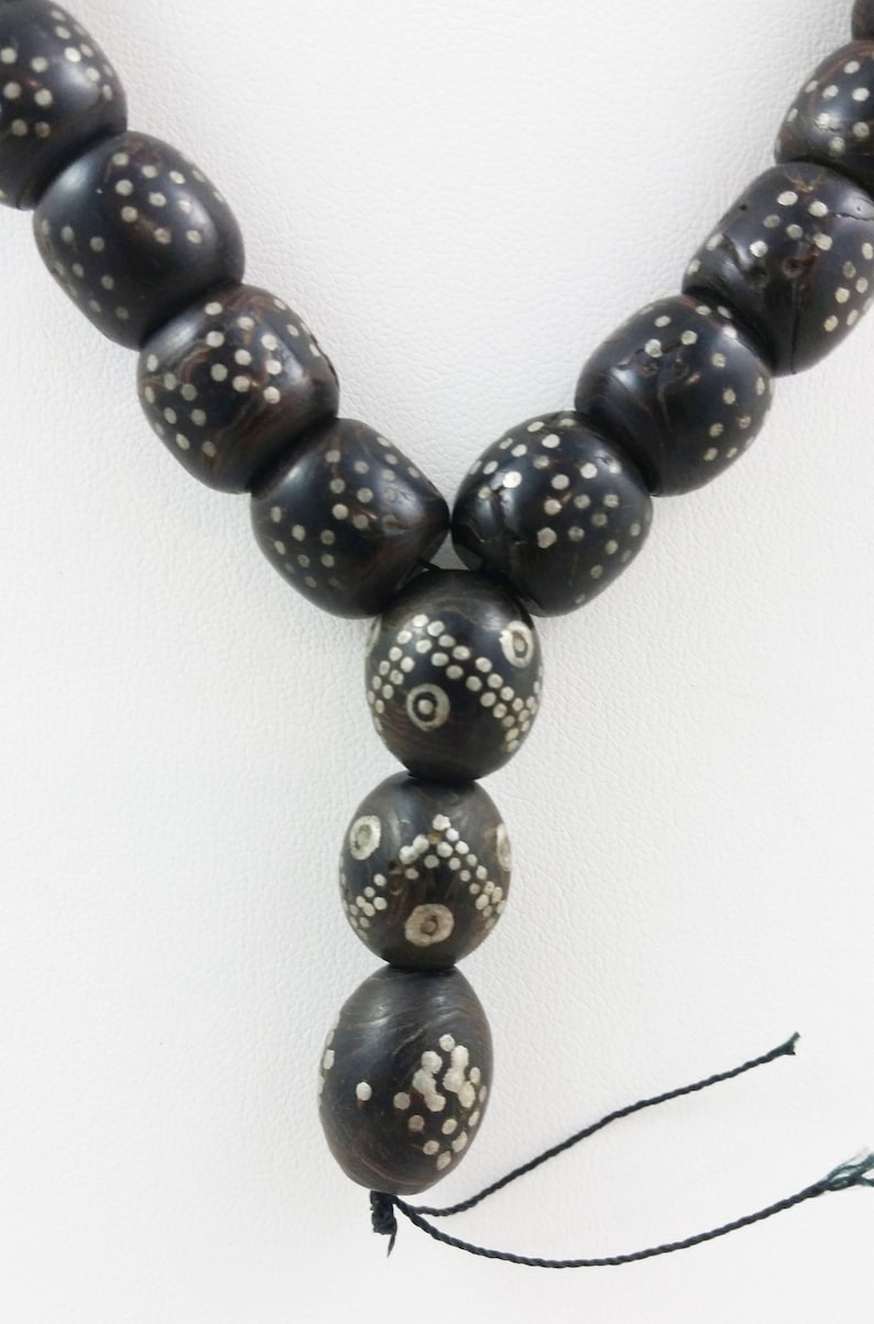 Pu&ograve; includere: Una collana di perline di legno nero con intarsi in argento. Le perline sono di forma ovale e hanno un motivo geometrico. La collana &egrave; infilata su un cordoncino nero.