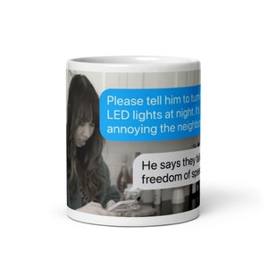 Könnte beinhalten: Eine weiße Keramiktasse mit einer blauen Textblase, die "Bitte sag ihm, dass er die LED-Leuchten nachts ausschalten soll. Es nervt die Nachbarn." und einer zweiten blauen Textblase, die "Er sagt, sie fühlen sich frei zu sprechen." sagt.