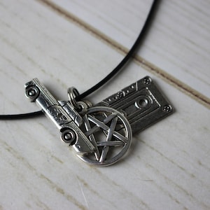 Może przedstawiać: Czarny sznurek z trzema srebrnymi zawieszkami: samochodem, pentagramem i kasetą.