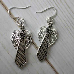 May include: Silver dangle earrings with a tie and angel wings design. The tie is black and white striped.