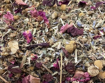 May include: A close-up of a blend of dried herbs and flowers, including lavender, chamomile, rose petals, and other botanicals. The mixture is a light brown color with hints of purple and pink.