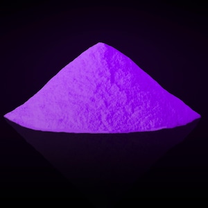 May include: A conical pile of fine, vibrant purple powder that glows with a bright, intense luminescence. The texture appears granular and soft, forming a sharp peak against a dark, solid black background, creating a high-contrast visual effect.