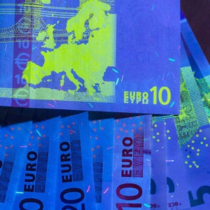 May include: A stack of ten euro bills illuminated with ultraviolet light. The bills glow a bright blue and yellow, revealing security features like a map of Europe and the denomination printed in yellow.