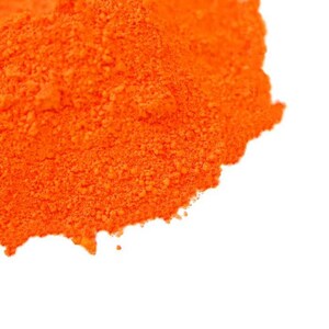 May include: A close-up of a pile of bright orange powder. The powder is finely ground and has a smooth, even texture.