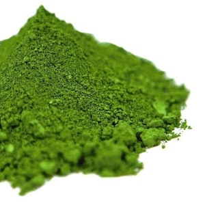 Può includere: Un mucchio di polvere fine di colore verde vibrante con una consistenza granulare. La sostanza è accumulata a punta, mostrando una tonalità smeraldo profonda e coerente su tutto il mucchio. Le particelle appaiono asciutte e irregolari.