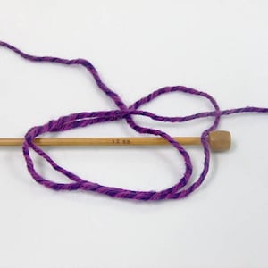 May include: Purple and pink yarn wrapped around a wooden knitting needle labeled "5.0 mm".
