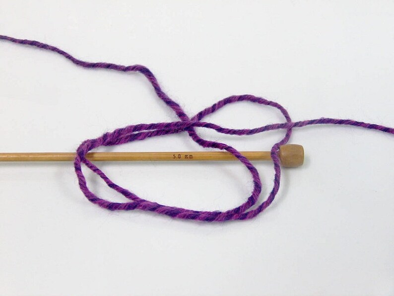 May include: Purple and pink yarn wrapped around a wooden knitting needle labeled "5.0 mm".