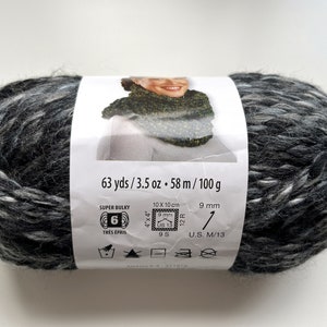 Puede incluir: Ovillo de lana s&uacute;per voluminosa en tonos grises y blancos. La etiqueta indica 58 metros, 100 gramos y recomendaciones de tama&ntilde;o de aguja. El grosor de la lana es 6.