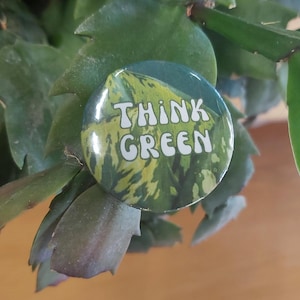 Könnte beinhalten: Ein grüner und gelber Knopf mit dem Text "Think Green" in weißen Buchstaben.