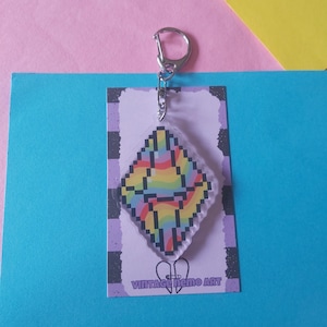 May include: A diamond-shaped keychain with a pixelated rainbow design. The keychain is attached to a silver clasp and hangs from a rectangular tag with the text "VINTAGE NEMO ART". The background is a mix of pink, blue, and yellow.