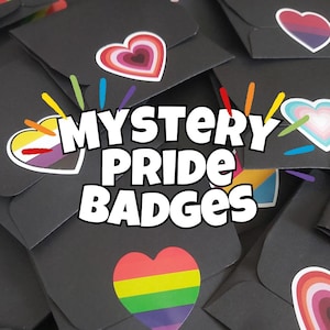 Puede incluir: Primer plano de sobres negros con pegatinas en forma de corazón de colores. Los sobres están etiquetados con "MYSTERY PRIDE BADGES".