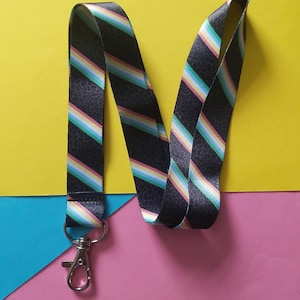 May include: A black and white striped lanyard with a rainbow stripe pattern. The lanyard has a silver metal clip.