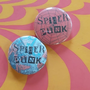 May include: Two circular badges with the words "SPIDER PUNK". One is red with a spiderweb design, the other is blue and red with a graphic design. The badges are on a pink and yellow background.
