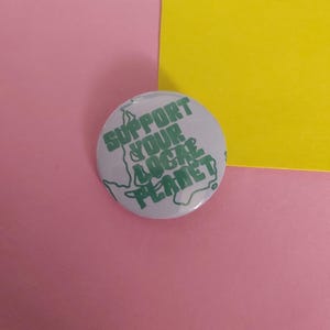 May include: A white button with a green outline of the Earth and the text "Support Your Local Planet" in green.