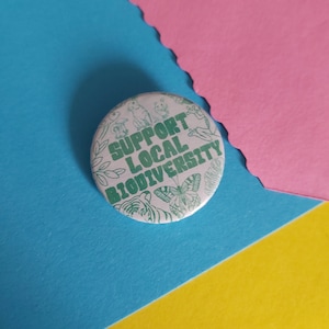 May include: A white button with a green outline and the text "Support Local Biodiversity" surrounded by illustrations of animals and plants.
