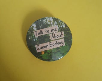 May include: A round button with a forest scene background. The button has text that reads "Talk to me About Queer Ecology".
