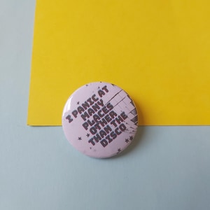 Puede incluir: Un botón blanco con texto negro que dice "I Panic At Many Places Other Than The Disco".