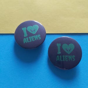 May include: Two black and green button badges with the text "I love aliens" and a green alien face inside a heart.