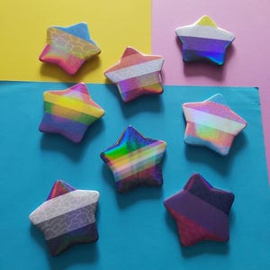 May include: Seven star-shaped decorative items with iridescent and patterned surfaces. The stars feature various color schemes, including rainbow stripes, and other designs. The stars are arranged on a colourful background of yellow, pink, and blue.