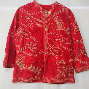 May include: A red jacket with gold embroidery featuring floral and abstract designs. The jacket has a mandarin collar, three-quarter sleeves, and two front pockets. It is buttoned up the front with gold buttons.