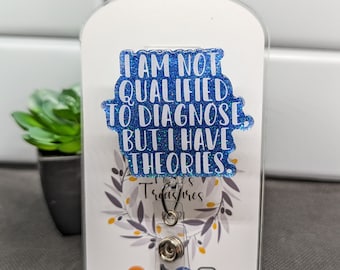May include: A blue glitter badge holder with the text "I am not qualified to diagnose, but I have theories."  The badge holder is on a white background with a small plant in the background. The badge holder has a silver clip and a small silver ring. The badge holder also has the text "Tillies Treasures" and social media icons.