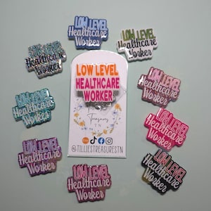 May include: Nine colorful, glittery, resin pins with the text "Low Level Healthcare Worker" in white lettering. The pins are arranged around a white card with the same text in orange lettering. The card also includes the text "Tillies Treasures TN" and social media icons.